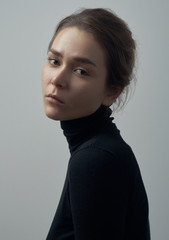 Dramatic portrait of a young beautiful girl with freckles in a black turtleneck on white background in studio - 129438675