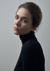 Dramatic portrait of a young beautiful girl with freckles in a black turtleneck on white background in studio - 129438681