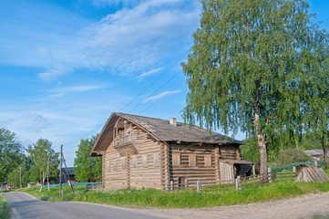 Fototapeta na wymiar Old wooden house with fretted balcony and nailed up windows on village street against blue sky background. Arkhangelsky region, Russia. 
