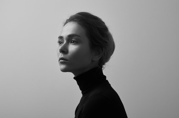 Dramatic black and white portrait of young beautiful girl with freckles in a black turtleneck on white background in studio - 129438810