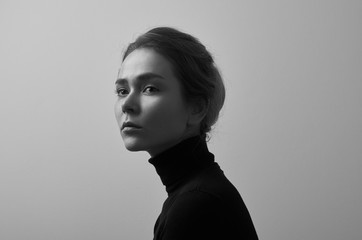 Dramatic black and white portrait of young beautiful girl with freckles in a black turtleneck on white background in studio - 129438821