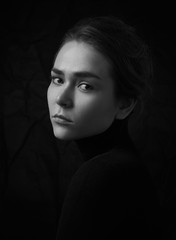 Dramatic black and white portrait of young beautiful girl with freckles in a black turtleneck on black background in studio