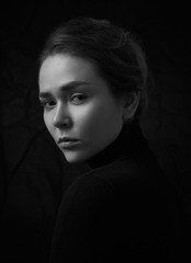 Dramatic black and white portrait of young beautiful girl with freckles in a black turtleneck on black background in studio