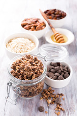 Homemade chocolate granola ingredients, nuts, oats, honey on white wooden background. Healthy breakfast concept.