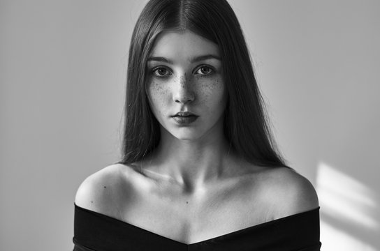 Dramatic black and white portrait of a beautiful lonely girl with freckles isolated on a white background in studio shot