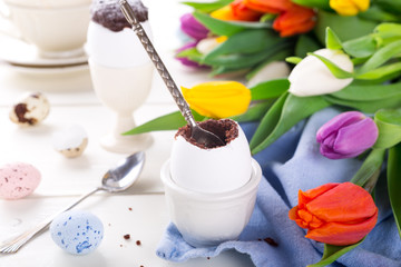 Easter egg filled with chocolate cake, tulips and colorful quail eggs on white background. Easter holidays breakfast concept.