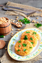 Fried pea patties on a plate. Spicy vegan patties cooked from yellow dried peas and decorated with parsley. Fork, knife, small decorative barrel on an old wooden background. Vegan food recipe. Closeup