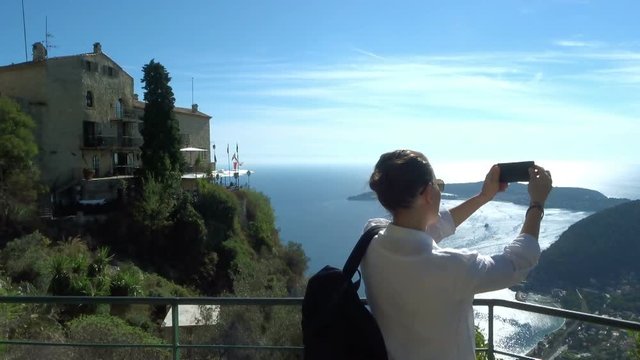 Young woman uses a smartphone to video a beautiful view at the sea, riviera coast