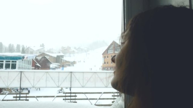 Beautiful young romantic girl looking through the window in mountain ski resort Sheregesh. 3840x2160