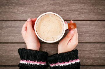 Little girl hand holding cup of hot coffee on wooden table
