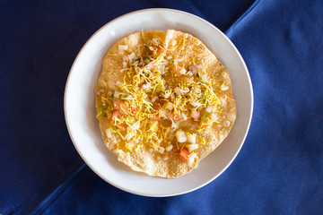 Indian food (Masala papad) on white dish with blue background