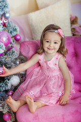 Fototapeta premium Happy cheerful little girl excited at Christmas Eve, sitting under decorated illuminated Tree. Greeting card or cover, horizontal with copy space.
