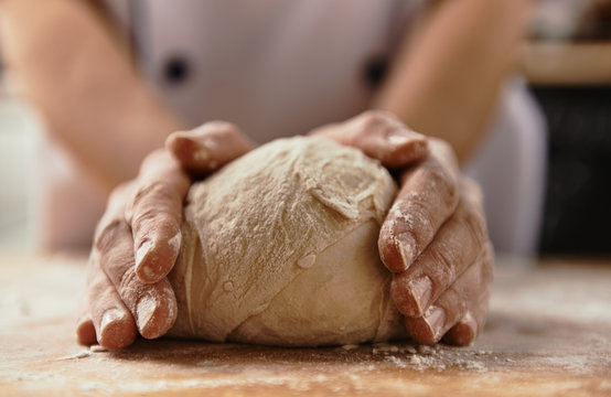 Close-up of chef hands kneading raw bread dough on wooden board.  