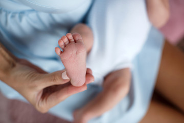 Happy woman,brunette,white mother of pearl nail Polish, gently hold in their palms a little pink feet newborn baby photo on a pink background in the bedroom