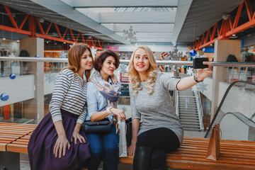 Group of cute girl friends doing some shopping at a mall and taking a selfie with a smartphone