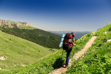 Fototapeta premium Hiking young woman with backpack and trekking poles on the mountain trail