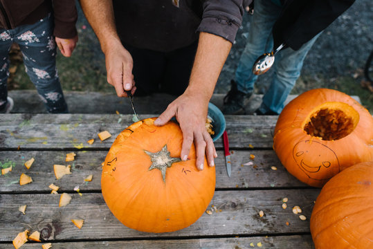 Children watching adult carve pumpkin, mid section