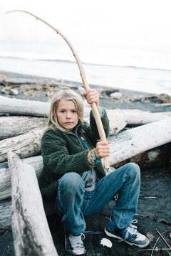 Portrait of boy at beach, leaning on driftwood, holding stick