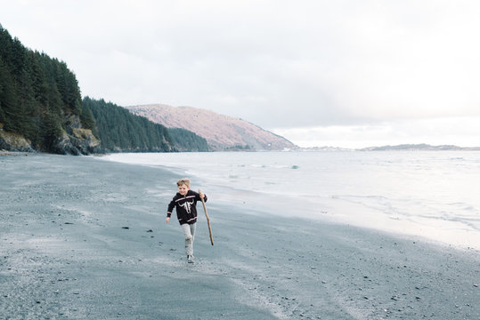 Boy running on beach, carrying driftwood