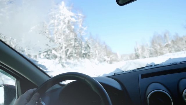 Man's hands of a driver on steering wheel in slow motion on winter landscape outdoors. 1920x1080