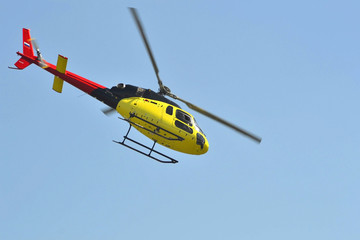 Fototapeta premium The small yellow helicopter flies in the sky.