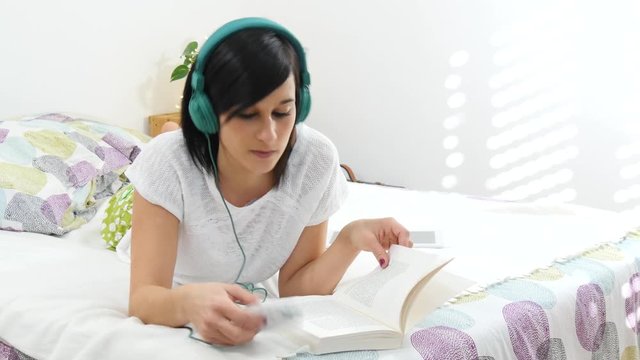 Beautiful young woman lying down on bed listen music with headphones