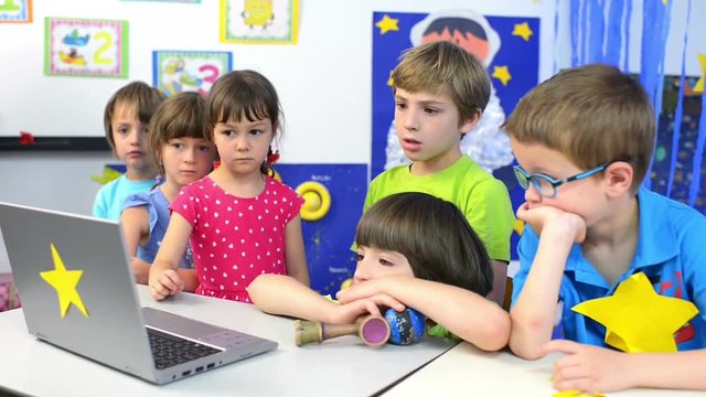 Expressive kids at kindergarten watching a movie at laptop
