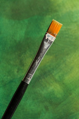 Single small paint brush in front of painted green background