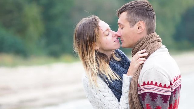 Young attractive couple in knitted sweaters on a cliff on sea shore, teasing, hugging and kissing