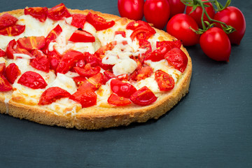 Fresh Italian bruschetta with roasted tomatoes, mozzarella cheese, olive oil and basil and oregano herbs on black plate background