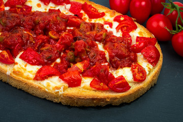 Fresh Italian bruschetta with roasted tomatoes, mozzarella cheese, olive oil and basil and oregano herbs on black plate background