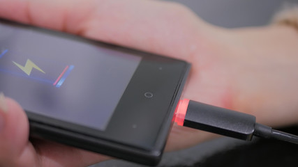 Woman's hand hold smartphone with low battery icon on screen - USB data cable connecting on modern gadget. Close up