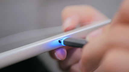 Woman's hand plugging black lightning charging cable into pc digital tablet - USB data cable connecting on modern gadget. Close up