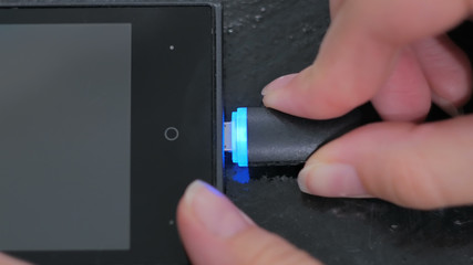 Woman's hand plugging black lightning charging cable into smartphone - USB data cable connecting on modern gadget. Close up