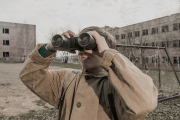 Boy with binoculars in hand. young boy stands near the abandoned building. abandoned city. wanderer...