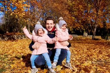Fototapeta premium Happy children with father in the park autumn outdoors, yellow leaves laughing, having fun, smiling clothing 