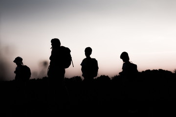 Fototapeta na wymiar Silhouette of family hiking at sunset. Happy big family on summer vacation in mountains. Mother and kids carry backpacks. Tourists walking on cliff edge.Summertime.Little children traveling.