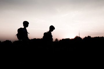 Fototapeta na wymiar Silhouettes of kids hiking at sunset. Happy boy and girl on summer vacation in mountains. Tourists walking on cliff edge carrying backpacks. Summertime. Little children traveling. Friendship concept.