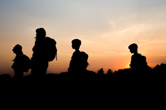 Silhouette of family hiking at sunset. Happy big family on summer vacation in mountains. Mom and kids carry backpacks. Tourists walking on cliff edge. Summertime. Little children traveling.
