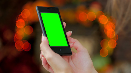 Woman using vertical smartphone with green screen. Close up shot of woman's hands with mobile. Elegant abstract garlands bokeh background