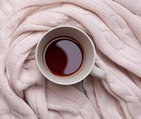 Black tea  in a ceramic cup wrapped around a warm knitted blanket