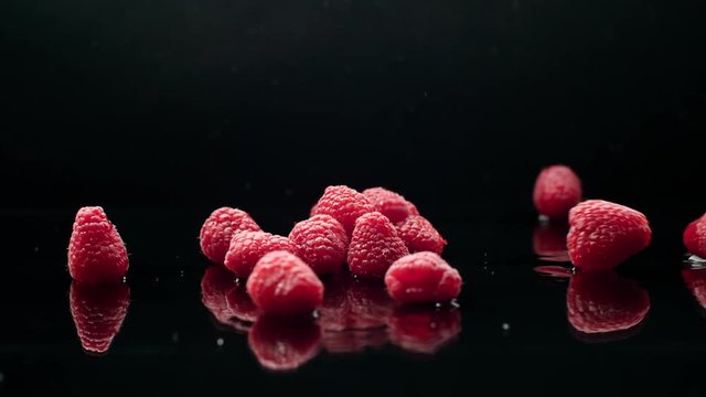 raspberry rain, luscious ripe berries fall from the water in slow motion, black background