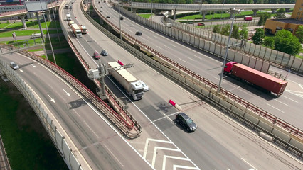 Aerial view at lines of city highway. Semitrailer trucks and cars drive on roads in small traffic jam. Russia