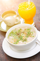 Boiled rice pork or mush with orange juice and hot coffee on wood table with sunlight.