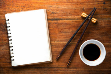recipe book with chopsticks and soy sauce bowl on wooden background. Top view with copy space