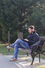 Naklejka na ściany i meble Side view portrait of a young man sitting on bench smiling at laptop
