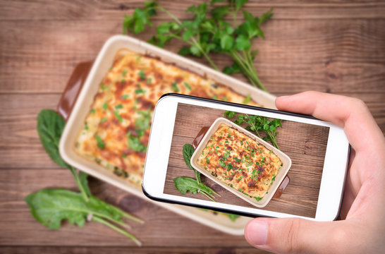 Hands taking photo chicken lasagna and white cheese with smartphone.