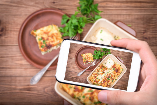 Hands taking photo chicken lasagna and white cheese with smartphone.