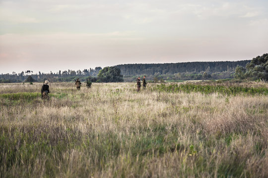 Hunting scene with hunters going through rural field during hunting season 