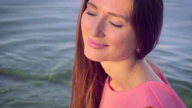 Charming white woman in a pink dress on a background of water.